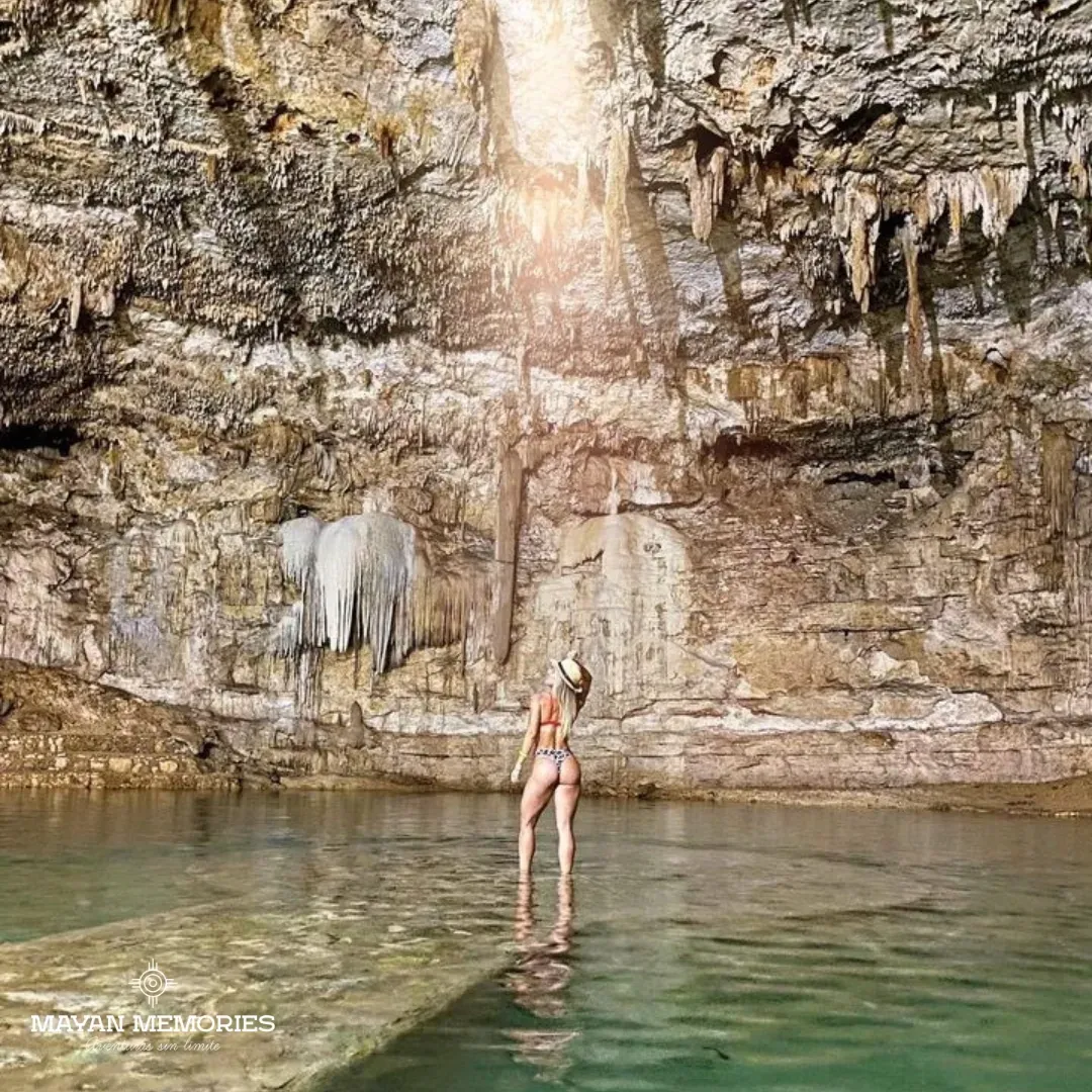 Visitante de pie en la plataforma de un cenote de caverna bajo un haz de luz