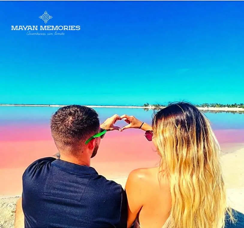 Couple making a heart with their hands in front of the pink lagoon at Las Coloradas