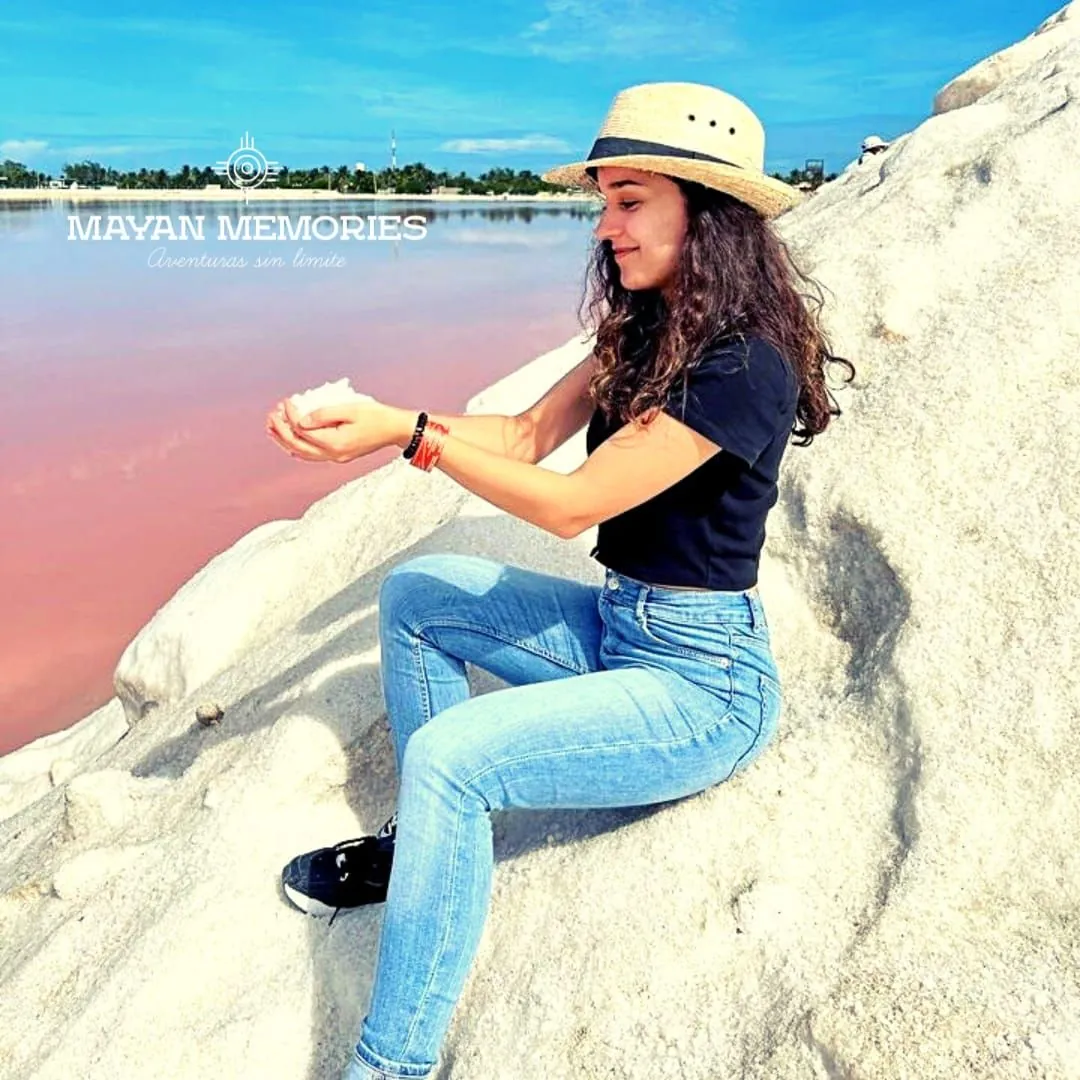 Woman in a hat sitting on a salt mound beside the pink water