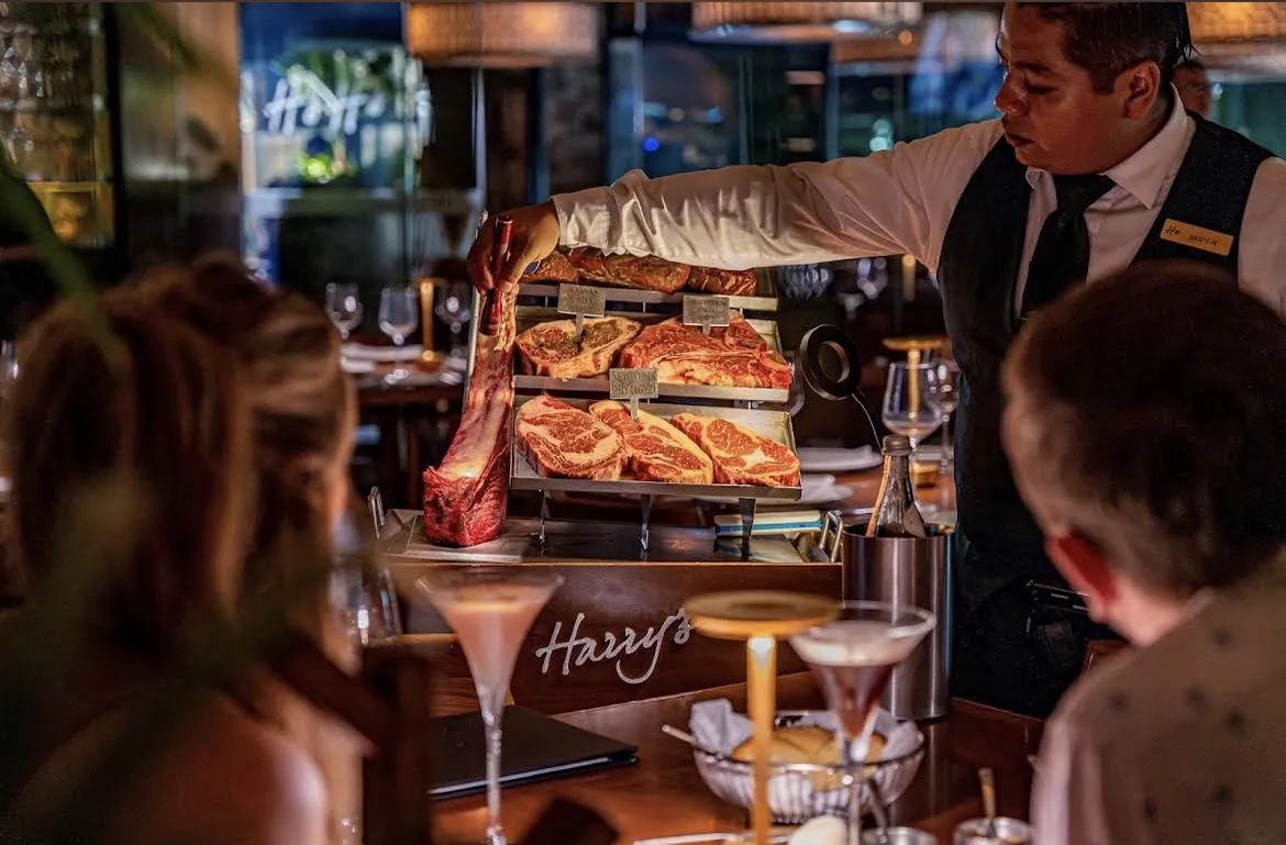 Mesero junto a la barra de Harry's con botellas iluminadas