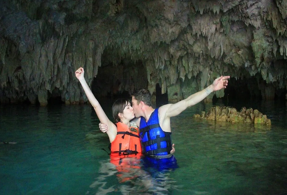 Couple in life jackets raising their arms in a cave cenote