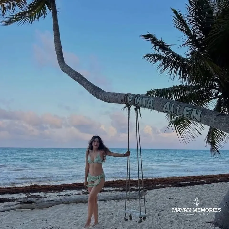 Mujer en un columpio colgado de una palmera en la playa