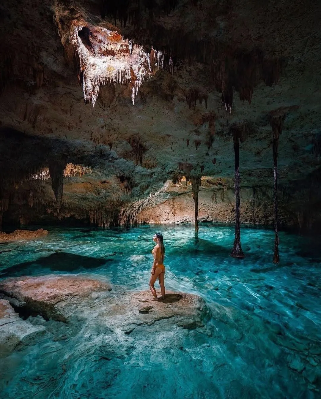 Mujer de pie en un cenote de caverna con estalactitas
