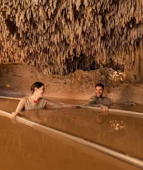 Two people submerged in a mud pool inside a cavern
