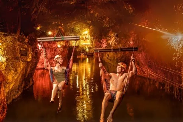 People on a zip line inside a lit cavern